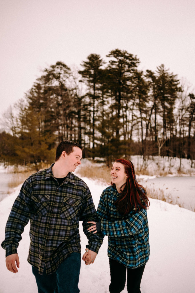 Couple laughing during their snowy engagement session in Moreau Lake State Park.
